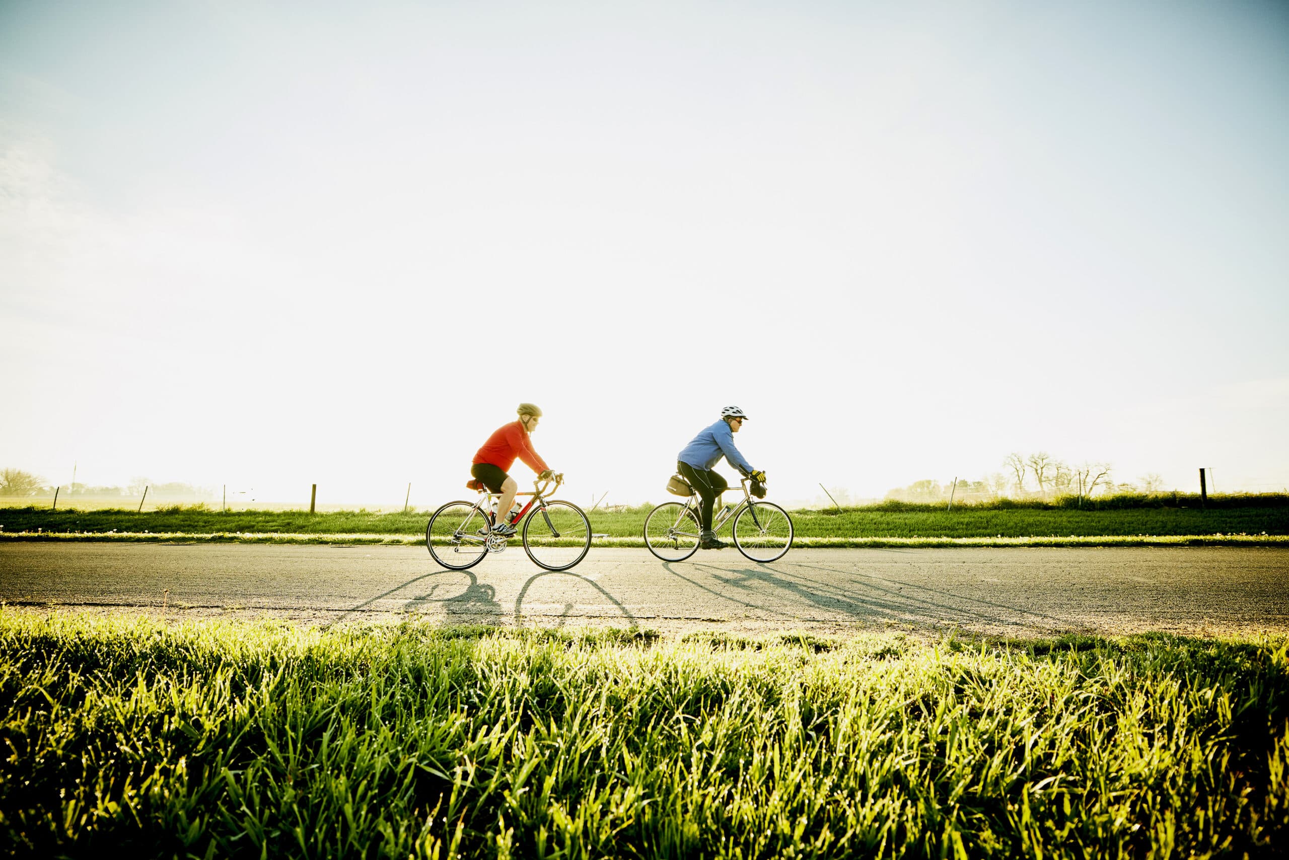 Wide shot of senior male friends on sunrise bike ride on rural road