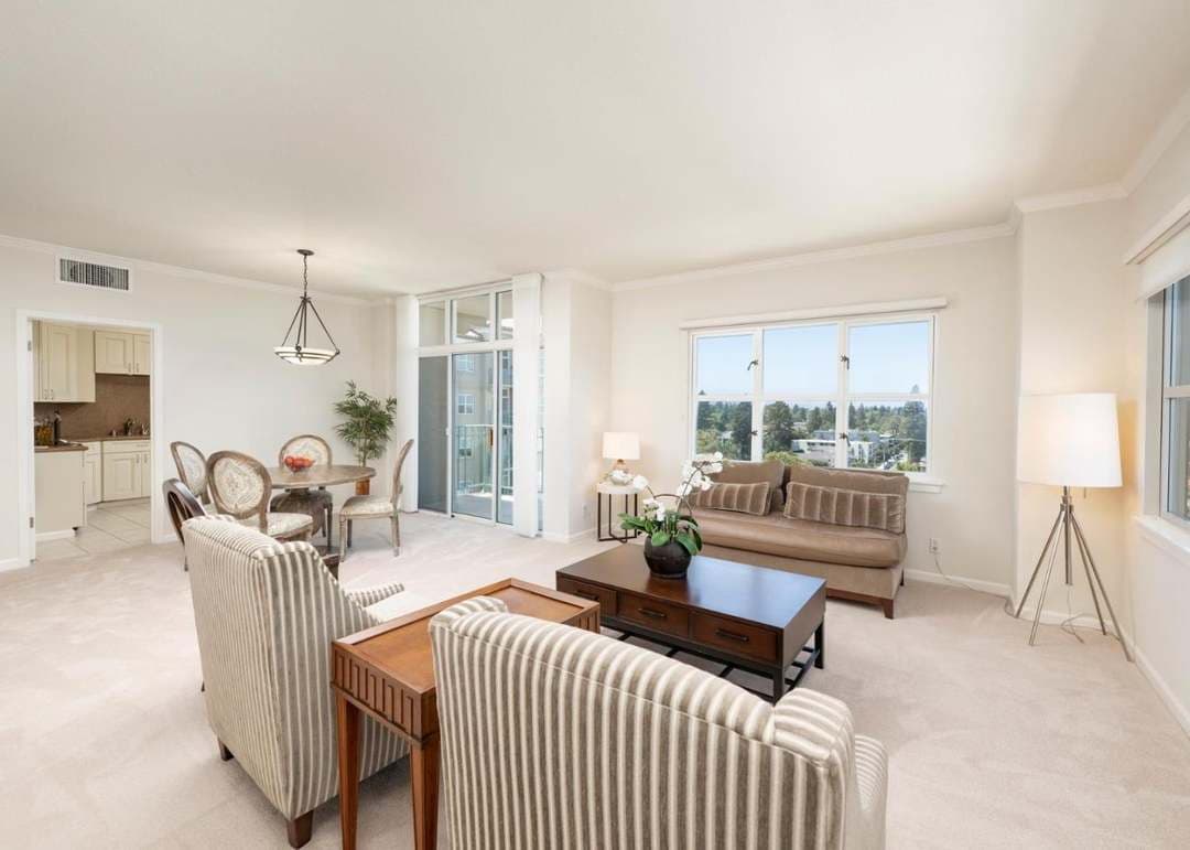 Living room with large windows, light carpet, couch, two chairs and views into the dining room